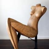 Die Holzskulptur ist Lebensgroß, sie sitzt auf einem stählernen Stuhl